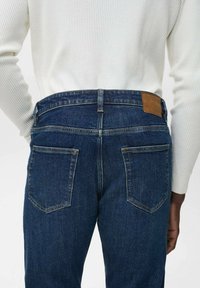 Dunkelblaue Denim-Jeans mit hoher Taille, ausgestattet mit einem braunen Lederpatch, zwei Gesäßtaschen und dezenten Nähten.