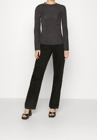 Mörkgrått ribbat tröja med långa ärmar, kombinerat med svarta vida byxor och grova svarta sandaler. Enkel, figurnära design och textur.