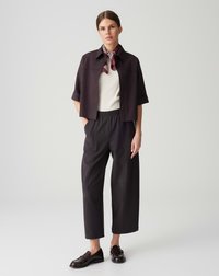 Black cropped jacket with short sleeves, paired with high-waisted dark trousers and a white top, accented by a striped scarf. Brown shoes.