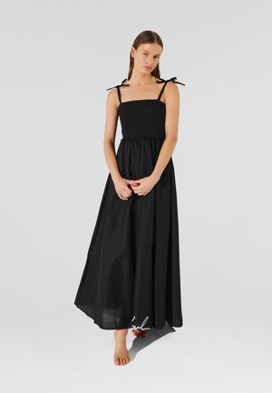 Black maxi dress with a smocked bodice, adjustable tie straps, and a flowing skirt. Made from lightweight fabric with a smooth texture.