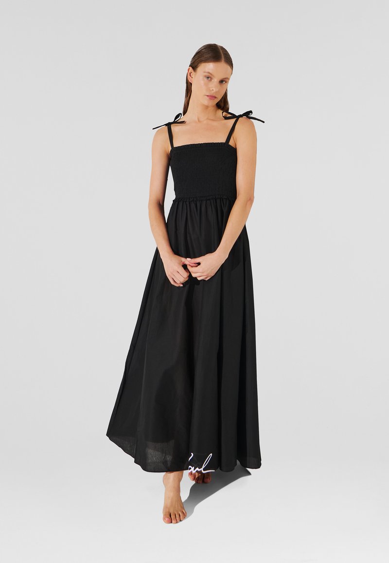 Abito maxi nero con corsetto arricciato, spalline regolabili e gonna fluida. Realizzato in tessuto leggero con una texture liscia.