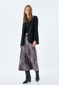 Zwart op maat gemaakte blazer over een ronde hals navy top, gecombineerd met een lange, vloeiende rok met luipaardprint en kniehoge zwarte blokhakken.