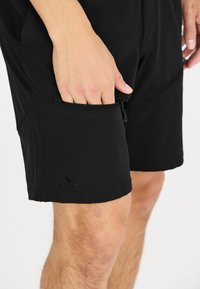 Svarta idrottsshorts gjorda av flexibelt material, med en dragkedjeficka och en logotyp i det nedre hörnet. Slät textur, knälång design.