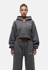 Grijze cropped hoodie met oversized mouwen, een rits aan de voorkant en een logo. Gecombineerd met bijpassende grijze sweatpants met elastische taille en logo-detail.