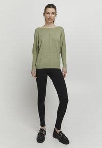 Oversized svetle zelený pletený svetr s lodním výstřihem, kombinovaný s černými ribbed legínami a masivními černými mokasíny.