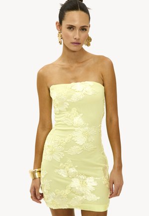 Robe sans bretelles jaune avec broderie florale, design ajusté et texture lisse. De grands accessoires dorés complètent la tenue.