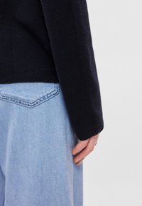 Σκούρο μπλε πλεκτό πουλόβερ με μανίκι δίπλα σε ανοιχτό μπλε τζιν με διακριτική υφή, διαθέτοντας σχέδιο ραφής στην πίσω τσέπη.