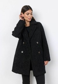 Abrigo negro texturizado de corte holgado, diseño de doble botonadura, grandes solapas y botones metálicos. Tejido acogedor con detalles de costura visibles.