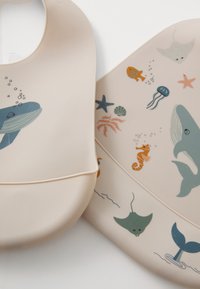Silicone bibs in soft beige, featuring underwater-themed illustrations like whales, jellyfish, and seahorses in blue, orange, and green tones.