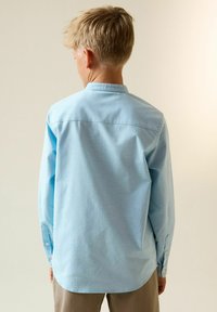 Hellblaues Langarmhemd mit Knopfkragen, Rückenpasse und geknöpften Manschetten. Weiche, glatte Stoffstruktur.