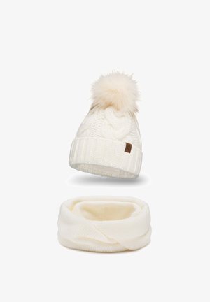 Hvid strikket hue med en faux fur pom-pom, der har et tekstureret kabeldesign og en tyk ribbet manchet. Nedenfor ses et matchende hvidt infinity-sjal.