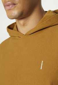 Felpa con cappuccio marrone in tessuto strutturato con cappuccio regolabile con coulisse. Presenta un piccolo logo "SANDRO" bianco sul petto. Design semplice.