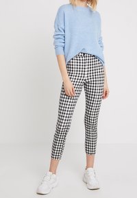 Pull bleu clair duveteux à manches longues, accompagné d'un pantalon court à carreaux noirs et blancs. Une paire de baskets blanches complète la tenue.