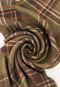 Tessuto morbido con motivo a quadri marrone, verde e arancione, disposto in una piega a spirale su sfondo bianco.