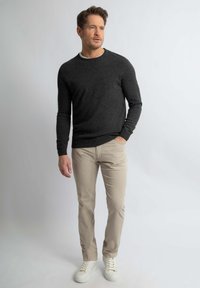Donkergrijze trui, lichtbeige broek en witte sneakers. De trui heeft een ronde hals en lange mouwen, gemaakt van zachte stof.