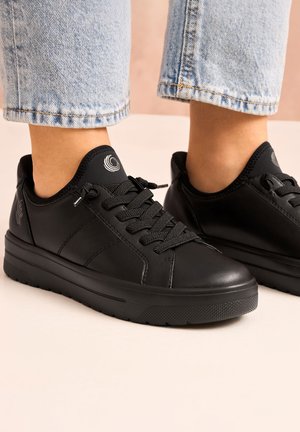 Baskets en cuir noir avec surface texturée, lacets noirs et logo rond sur le talon. Présente une semelle épaisse et des accents cousus.
