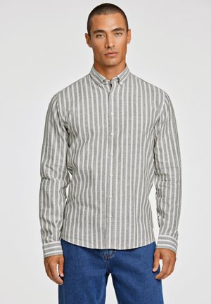 Camisa de botones a rayas grises y blancas con mangas largas, que presenta un cuello y un dobladillo recto, combinada con pantalones de mezclilla azules.