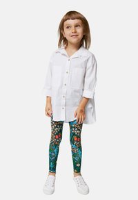 Fehér, gombos ing, két zsebekkel, színes virágmintás leggings-el és fehér sportcipővel párosítva.