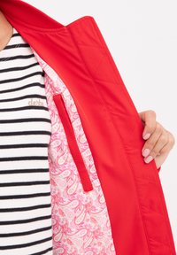 Röd vadderad jacka med en rosa paisleymönstrad foder. Inre ficka synlig. Lager på lager med en topp med svart-vita ränder.