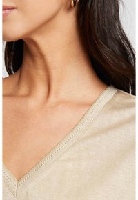 Beige V-hals top met fijne ribgebreide afwerking, een gladde textuur en een subtiele glans, die de halslijn en schouderregistratie benadrukt.