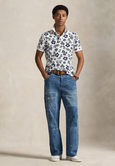 Λευκό πόλο πουκάμισο με ναυτικό φλοράλ μοτίβο, συνδυασμένο με ξεθωριασμένο μπλε τζιν παντελόνι με πιτσιλιές χρώματος και τσέπες τύπου καρό. Λευκά αθλητικά παπούτσια.