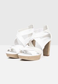Sandales blanches à talons avec des lanières croisées, texture lisse, bout ouvert et un talon en bois clair avec des rainures horizontales.