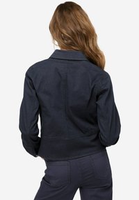 Tmavě modrá džínsová bunda s upraveným střihem, klasickým límcem, dlouhými rukávy a detaily šití. Zadní pohled ukazuje hladkou texturu.