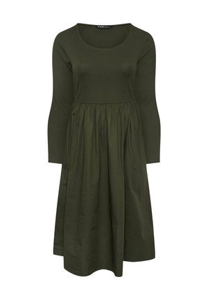 Pitkähihainen oliivinvihreä mekko, jossa on istuva ribbikangasrunko, pyöreä kaula-aukko ja keskeltä kerätty hame, joka ulottuu puoliväliin pohkeita.