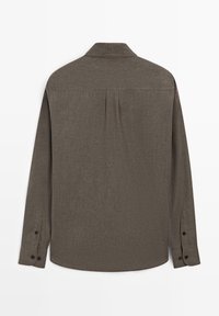 Brun langærmet skjorte med krave, der har et læg bagpå og manchetter med knapper, lavet af tekstureret stof med et diskret mønster.