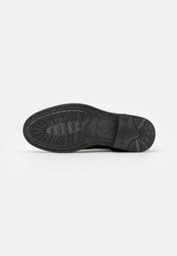 Suela de zapato de goma negra con superficie texturizada, que presenta un patrón de banda de rodadura para mayor agarre y acentos circulares. Tacón reforzado y detalles laterales visibles.
