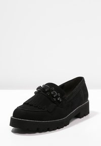 Svart mocka loafers med fransdesign, prydda med svarta stenar på fronten och en tjock, texturerad gummisula.