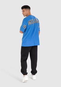 Camiseta azul con letras negras "MILORD" en la parte posterior, combinada con joggers negros y zapatillas blancas. Tela suave y corte relajado.