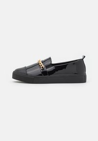 Black patent slip-on shoes with a rounded toe, featuring a gold chain detail across the vamp and a textured rubber sole.