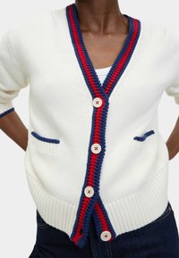 Cardigan bianco con rifiniture a coste rosse e blu navy, dotato di maniche corte, tasche frontali e grandi bottoni con dettagli rossi.