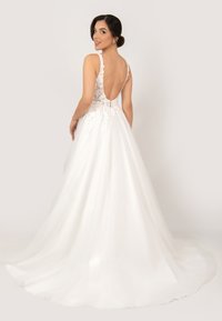 Weißes Hochzeitskleid mit tiefem V-Rücken, das aufwendige florale Spitzen-Details und einen fließenden Tüllrock aufweist. Glatte Textur und elegantes Design.