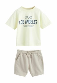 Ljusgul bomullströja med marinblå tryck "LOS ANGELES" och två smiley-ansikten; tillsammans med beige sweatshorts med fickor och elastisk midja.