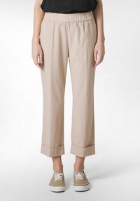 Beige, kevyet, kapenevat housut, joissa on joustava vyötärö ja käännetyt lahkeet. Kangas vaikuttaa sileältä ja siinä on hieman kiiltoa. Yhdistetty beigeihin lenkkarikenkiin.