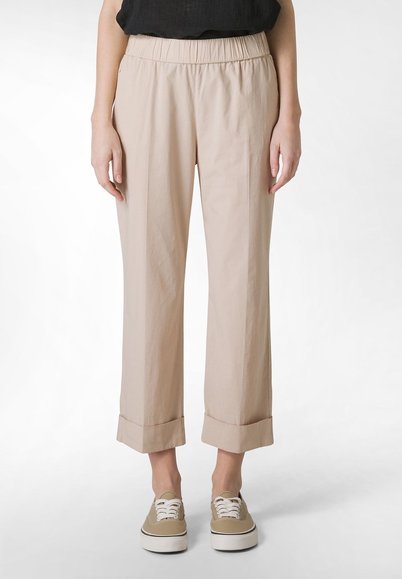 Beige, kevyet, kapenevat housut, joissa on joustava vyötärö ja käännetyt lahkeet. Kangas vaikuttaa sileältä ja siinä on hieman kiiltoa. Yhdistetty beigeihin lenkkarikenkiin.