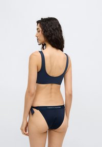 Σετ μπικίνι σε ναυτικό μπλε με τοπ με στρογγυλεμένη πλάτη και ψηλόμεσο σλιπ με κορδόνια στο πλάι, κατασκευασμένο από απαλό ύφασμα με λωρίδα λογότυπου στη μέση.