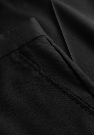 Sort stof tæt på med et linning og en lomme. Materialet er glat med en let glans og rene, præcise syningsdetaljer.