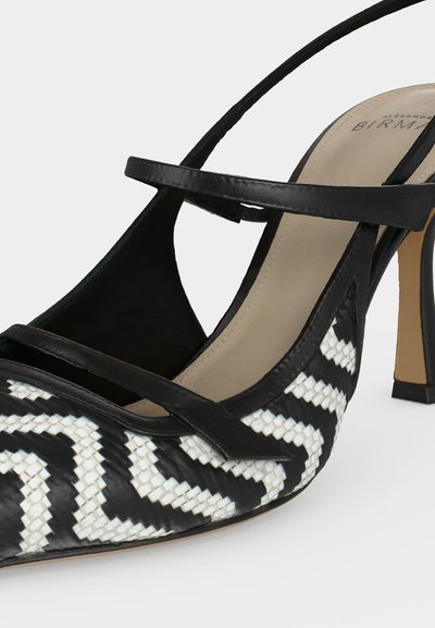 Escarpin à talon haut tissé noir et blanc à bout pointu avec fines lanières noires et semelle intérieure beige sur fond blanc.