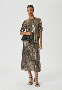Set metallico dorato con paillettes, composto da una maglietta a maniche corte e una gonna midi. Abbinato a una borsa a tracolla nera e sandali neri con strappi.