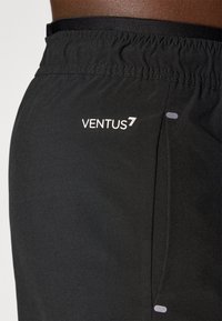 Crne atletske kratke hlače s elastičnim pojasom, koje sadrže bijeli logo "VENTUS7" i mali sivi naglasak na strani. Glatka tekstura.