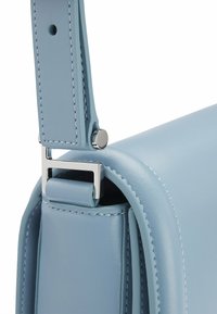 Dettaglio di una borsa in pelle azzurro chiaro con una forma strutturata, hardware in argento, cuciture eleganti e una fascia larga regolabile.