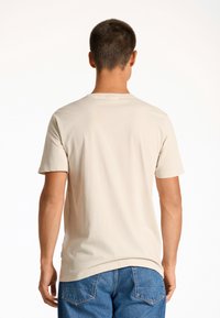 Camiseta beige de manga corta con escote redondo, textura suave y corte relajado, combinada con unos vaqueros azules de mezclilla con bolsillos traseros.