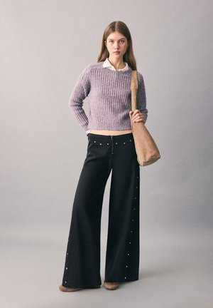 Suéter de punto lavanda, pantalones de pierna ancha negros con detalles de tachuelas y un bolso de hombro color marrón claro. Textura suave, corte relajado y diseño moderno.