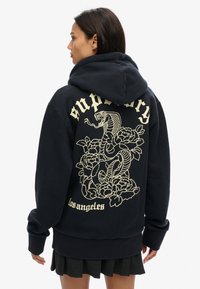 Sudadera azul marino en mezcla de algodón con un gran diseño de serpiente amarilla y flores en la parte posterior, que incluye el texto "supremacía los ángeles."