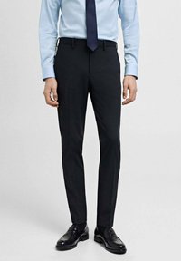 Svarta formella byxor med skräddarsydd passform, med bältesloopar, sidofickor och en slät yta, tillsammans med svarta loafers.