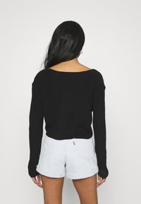 Schwarzer Strickpullover mit weitem Kragen und langen Ärmeln, kombiniert mit hellen Denim-Shorts mit umgeschlagenen Säumen und Rückentaschen.