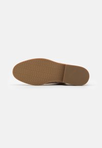 Semelle de chaussure en caoutchouc avec une surface texturée présentant un motif en arête de poisson, de couleur brun clair avec un bord lisse et plat.